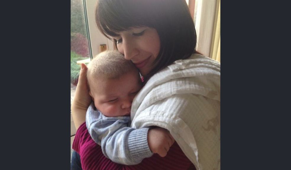 A mother lovingly cuddles her baby son with her hand cradling his head. Both have eyes closed.