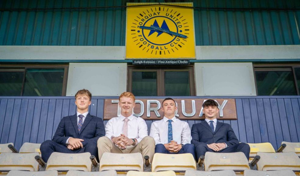 (Left to right) Toby Hard, Coby White, Fin Herbert and Jonah Shaw sit together in the stands at Torquay United Football Club, framed beneath the club’s crest. 