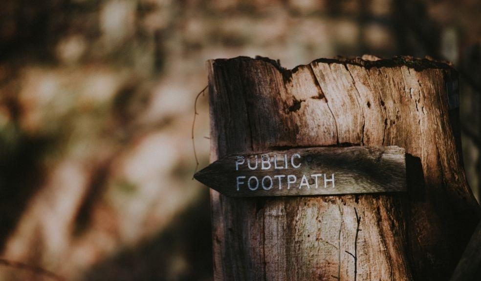 A photograph of a public footpath sign nailed to a tree stump, with woodland behind