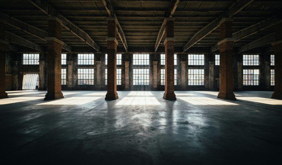 An empty industrial warehouse interior with brick columns, a concrete floor, and tall windows letting in light
