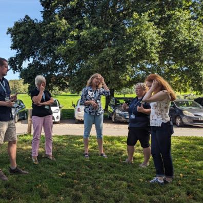 A group of people stand outside at Saltram listening to the instructor 