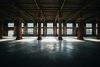 An empty industrial warehouse interior with brick columns, a concrete floor, and tall windows letting in light